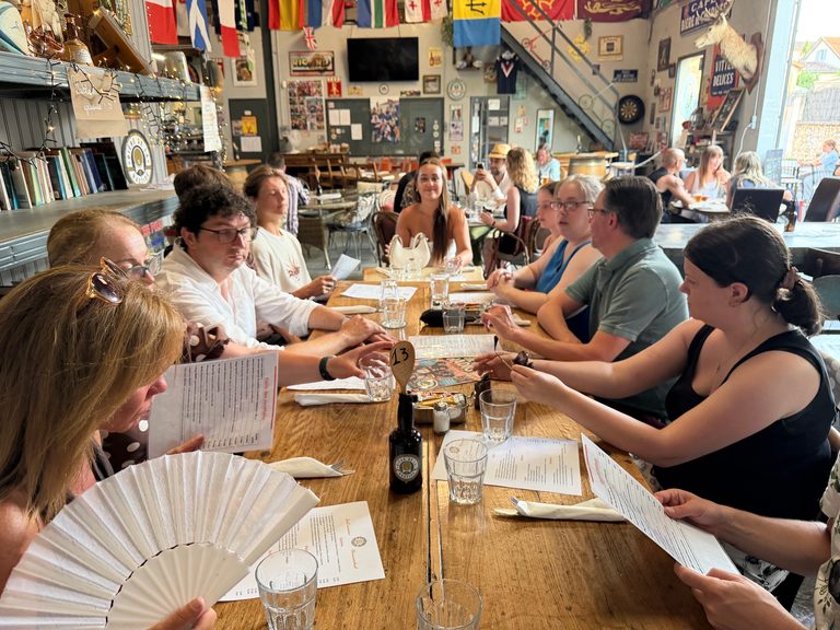 Gasten rond een houten tafel onder vlaggen bij Bière de la Bastide in Monpazier