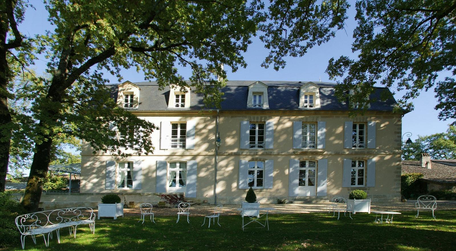 Château Bélingard’s pale façade and white shutters beneath trees in Pomport