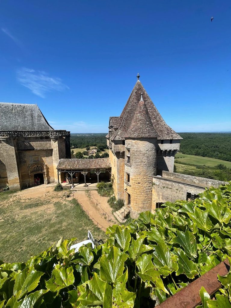 Stenen torens en binnenplaats van Château de Biron, met het beboste landschap van de Dordogne op de achtergrond