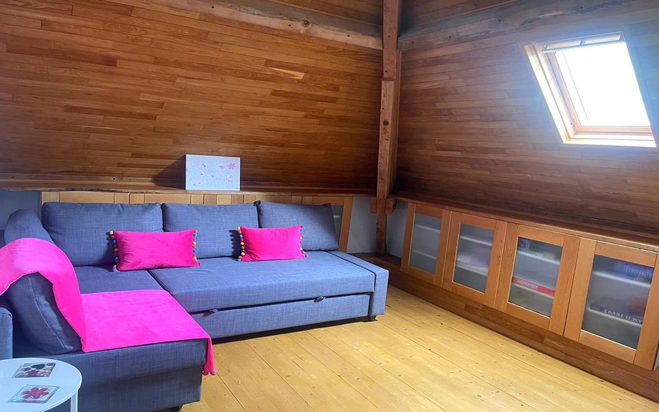 Ecksofa mit rosa Kissen im holzverkleideten Dachraum unter einem Dachfenster