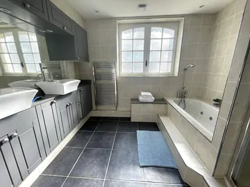Tiled bathroom with twin basins, a bath and shower screen beside the window