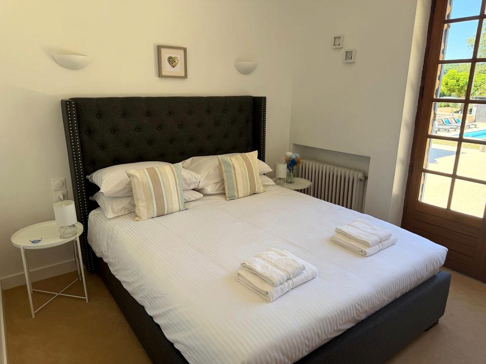 Doppelbett mit dunklem gepolstertem Kopfteil neben einer Glastür zur Terrasse