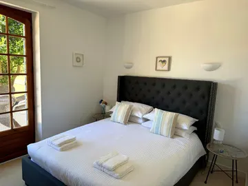 Double bed with a dark buttoned headboard and striped cushions beside a glazed door overlooking the garden