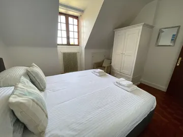 Double bed beneath a sloping ceiling, with a window and a tall white wardrobe