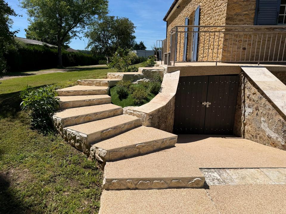 Geschwungene Steintreppe zwischen Rasen und Terrasse neben dem Haus