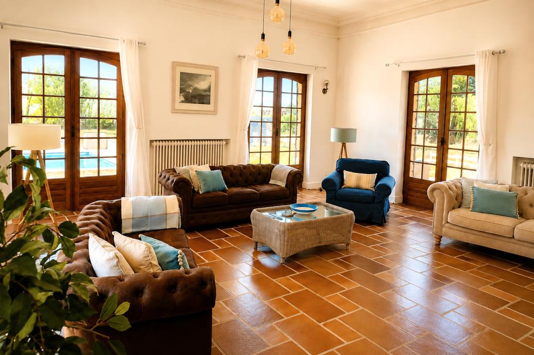 Sofas and a blue armchair around a coffee table, with terracotta floors and French doors to the garden