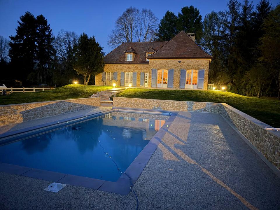 Beleuchtetes Steinhaus und blaues Poolwasser unter dem Abendhimmel