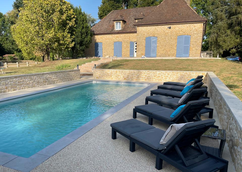Dunkle Sonnenliegen am türkisfarbenen Pool, dahinter die Steinfassade und blauen Fensterläden von Maison Sérénité