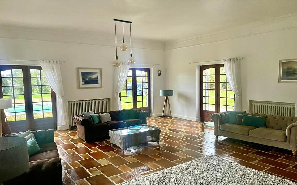Sofas um einen geflochtenen Couchtisch im Wohnzimmer mit Terrakottaboden und Fenstertüren