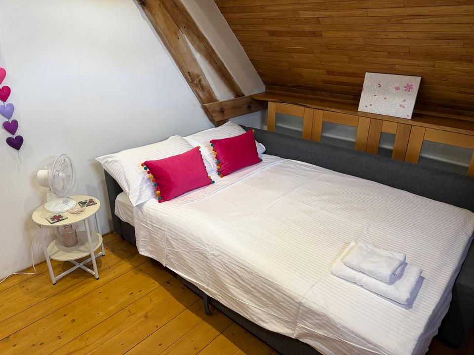 Ausgezogenes Schlafsofa mit weißer Bettwäsche und rosa Kissen unter der schrägen Holzdecke von Maison Sérénité