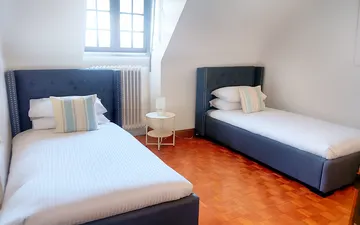 Two single beds with blue upholstered frames beneath a dormer window, on a parquet floor