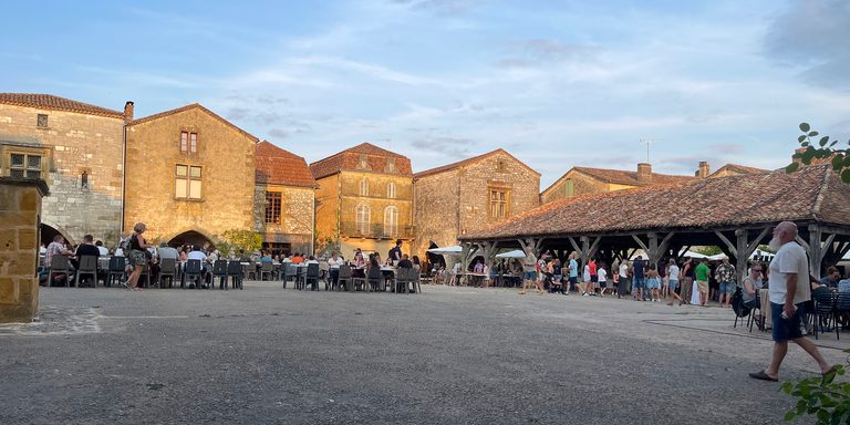 Mensen eten naast de overdekte markthal in Monpazier terwijl de avondzon de stenen gevels verlicht