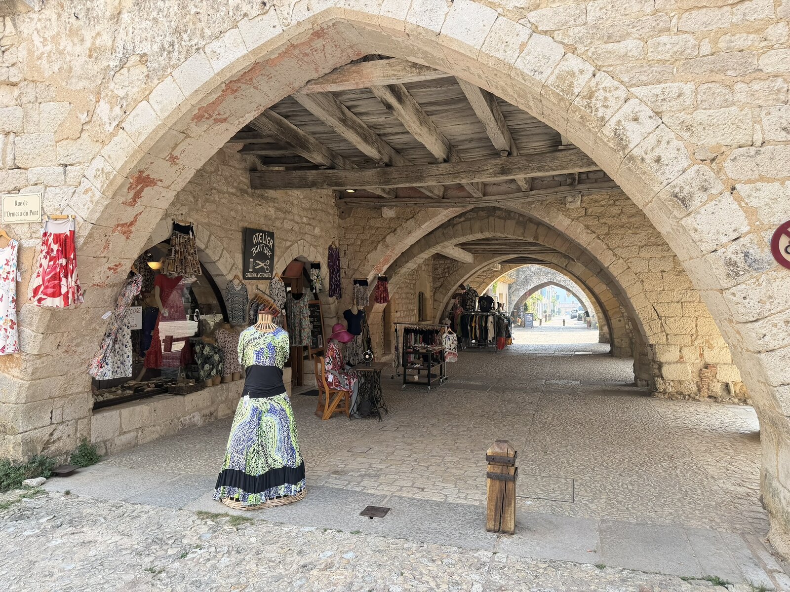 Covered stone passage and shopfront beneath the arcades of Place des Cornières in Monpazier